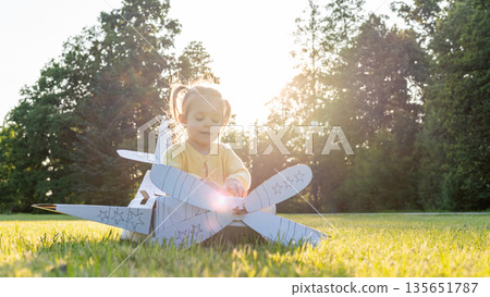 Cardboard airplane. Child pilot play outdoor. Toddler costume girl field yellow. Cardboard airplane. Child pilot play outdoor. Toddler costume girl field yellow. 135651787