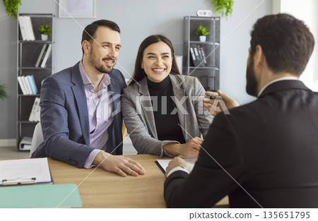Agent and couple of clients, businesspeople sitting, talking, discussing, gesturing, smiling 135651795