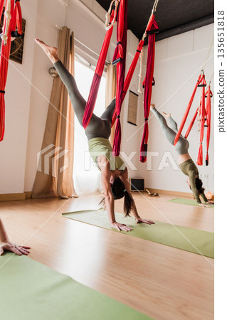 Women practicing aerial vinyasa yoga inversion in studio Women practicing aerial vinyasa yoga inversion in studio 135651818