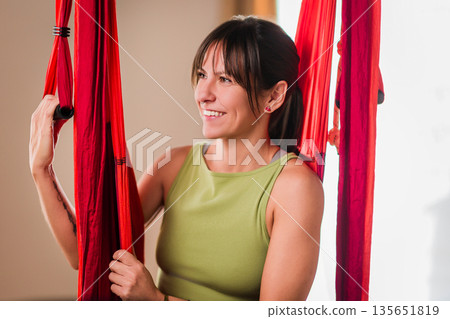 Woman smiling during aerial yoga hammock workout Woman smiling during aerial yoga hammock workout 135651819