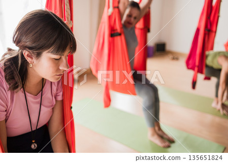 Women practicing aerial yoga in fitness studio 135651824