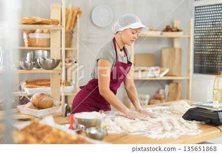 Girl works as baker in bakery, molds sausages from dough, rolls long round strips from dough 135651868