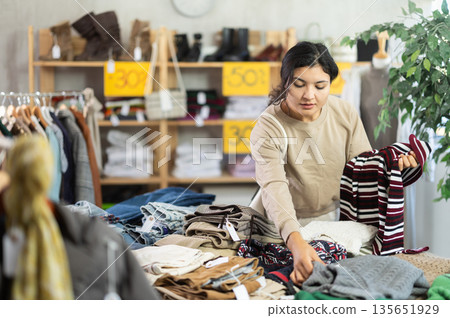 Latin girl is busy looking at clothes items in store, choose sweater Latin girl is busy looking at clothes items in store, choose sweater 135651929
