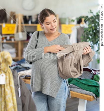 Pregnant european young female client choosing new trousers in clothing mall 135651942