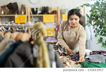 Latin girl is busy looking at clothes items in store, choose sweater 135651957