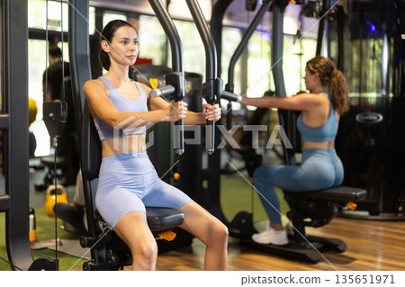 Sportive young girl training on chest fly machine in gym Sportive young girl training on chest fly machine in gym 135651971