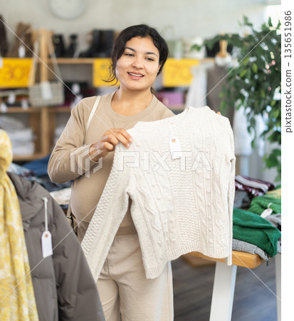 Interested positive pregnant latina young woman shopping sweaters in store. Sale of winter clothing collection 135651986