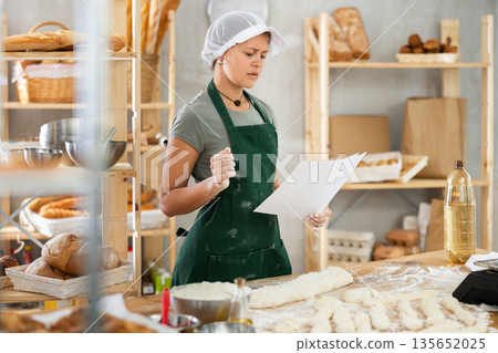 Young female baker read a new recipe on paper in the kitchen of private bakery Young female baker read a new recipe on paper in the kitchen of private bakery 135652025