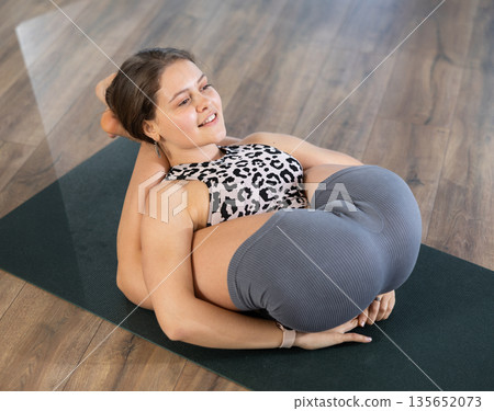 Pawanmuktasana yoga pose performed by slender girl in gym Pawanmuktasana yoga pose performed by slender girl in gym 135652073