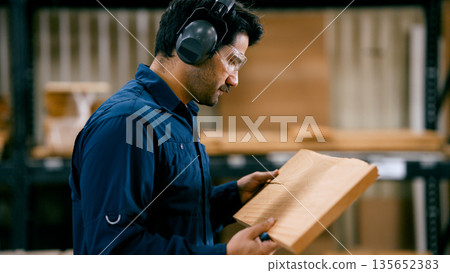 Carpenter inspecting wood plank in workshop Carpenter inspecting wood plank in workshop 135652383