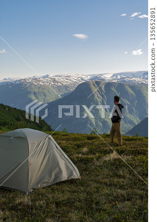 Hiker standing by tent admiring mountain view, Norway Hiker standing by tent admiring mountain view, Norway 135652891