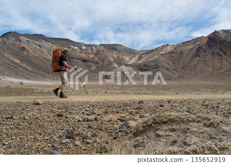 Hiker walking across arid volcanic crater floor in Tongariro National Park, NZ Hiker walking across arid volcanic crater floor in Tongariro National Park, NZ 135652919