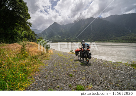 Male cyclist standing with loaded touring bike on gravel riverbed, New Zealand 135652920