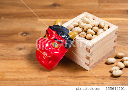 Setsubun beans in a wooden box and a red demon mask Japanese event on a wood grain background 135654201