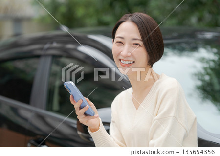 A woman standing in front of a car looking at her smartphone A woman standing in front of a car looking at her smartphone 135654356