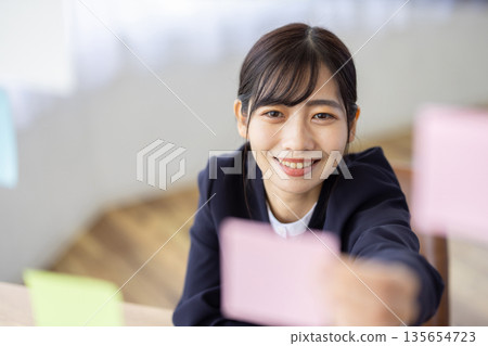 A young woman in a suit smiling with a sticky note in her hand in the office A young woman in a suit smiling with a sticky note in her hand in the office 135654723