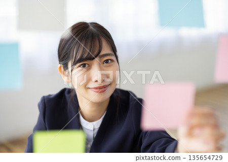 辦公室裡，一位身穿西裝的年輕女子麵帶微笑，手裡拿著一張便條紙。 135654729