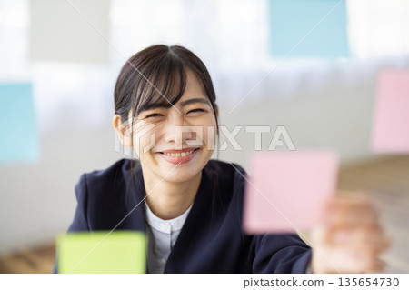 辦公室裡，一位身穿西裝的年輕女子麵帶微笑，手裡拿著一張便條紙。 135654730
