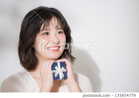 A smiling woman holding a White Day gift or present. An image of a thank you gift for an event or gift. A smiling woman holding a White Day gift or present. An image of a thank you gift for an event or gift. 135654779