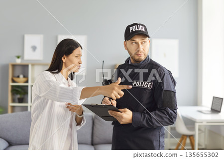 Male policeman listening to worried woman witness or victim of house burglary during investigation. Male policeman listening to worried woman witness or victim of house burglary during investigation. 135655302