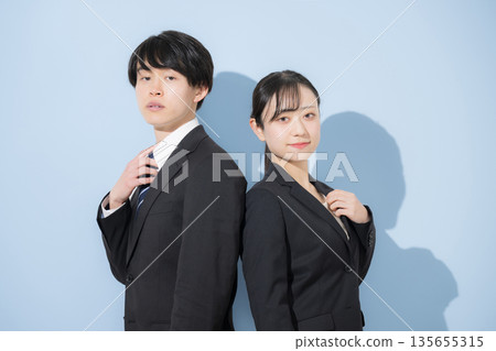 年輕的商務人士,如同大學生一般,背對背站在淺藍色背景前。招聘應屆畢業生和就業人員。 年輕的商務人士,如同大學生一般,背對背站在淺藍色背景前。招聘應屆畢業生和就業人員。 135655315
