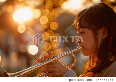 A young woman playing the trumpet in the setting sun 135655433