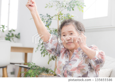 An elderly woman raising both hands in a fist pump. An image of health and stretching to feel refreshed. An elderly woman raising both hands in a fist pump. An image of health and stretching to feel refreshed. 135655586