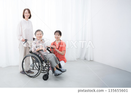 Nurses supporting elderly wheelchair-bound patients and their families in hospitals and home care facilities. Full-body view of the patient. Home and short-stay care. Nurses supporting elderly wheelchair-bound patients and their families in hospitals and home care facilities. Full-body view of the patient. Home and short-stay care. 135655601