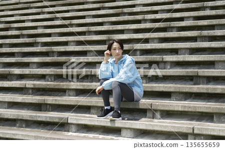 Sportswoman sitting on outdoor stairs Sportswoman sitting on outdoor stairs 135655659