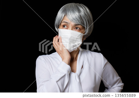 一位戴著口罩的老婦人斜向上看。 135655889