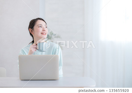 Woman drinking coffee while using a computer Woman drinking coffee while using a computer 135655920