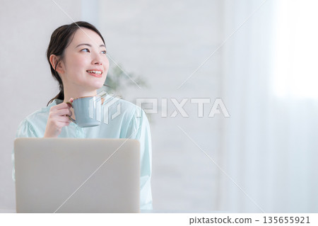 Woman drinking coffee while using a computer Woman drinking coffee while using a computer 135655921