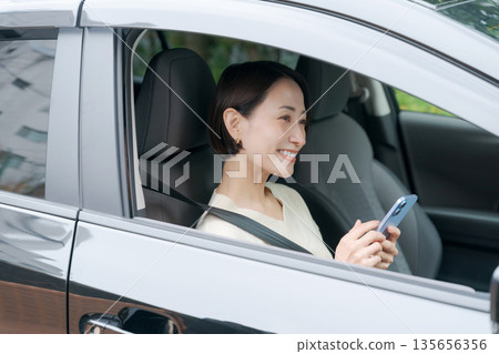 一名女子坐在駕駛座上看著她的智慧型手機 135656356