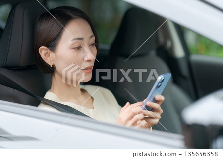 A woman looking at her smartphone in the driver's seat A woman looking at her smartphone in the driver's seat 135656358