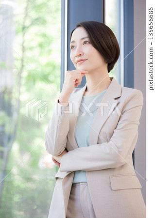 A businesswoman thinking by the window, worried about her career, what should she do about changing jobs? 135656686