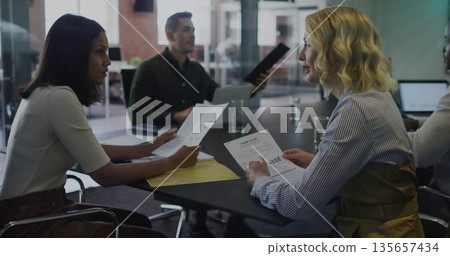 Reviewing printed reports four professionals meeting at table in office, with laptop and folder Reviewing printed reports four professionals meeting at table in office, with laptop and folder 135657434