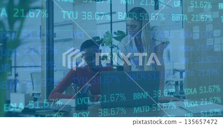 Two women collaborating writing in notebook and reviewing laptop in office, with pen holder plant Two women collaborating writing in notebook and reviewing laptop in office, with pen holder plant 135657472