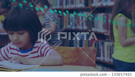 Girl in striped T-shirt reading open book at wooden table in library, with bookshelves, copy space 135657483