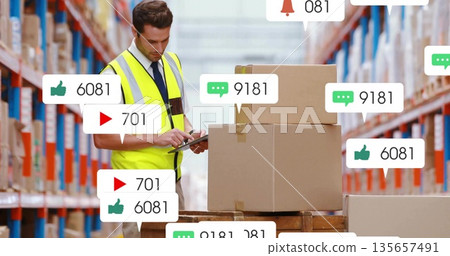 Worker wearing safety vest checking tablet beside pallet boxes in storage area, with notifications Worker wearing safety vest checking tablet beside pallet boxes in storage area, with notifications 135657491