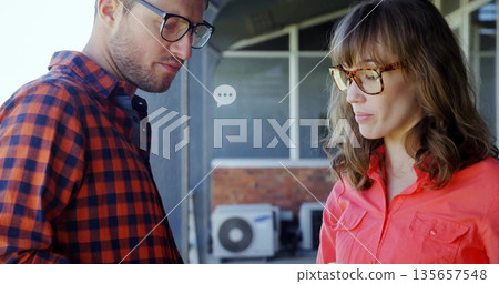 Discussing repair details two coworkers standing on exterior veranda, with AC condenser unit Discussing repair details two coworkers standing on exterior veranda, with AC condenser unit 135657548