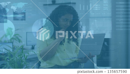 Sitting woman wearing work attire holding laptop and resting chin in office with monitors, plants Sitting woman wearing work attire holding laptop and resting chin in office with monitors, plants 135657590