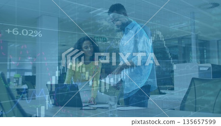 Collaborating woman in yellow top and man analyzing data at office desk with laptop and documents 135657599