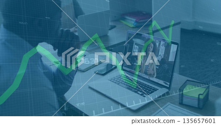 Man hosting online call at desk, with laptop phone tablet and green financial graph overlay Man hosting online call at desk, with laptop phone tablet and green financial graph overlay 135657601