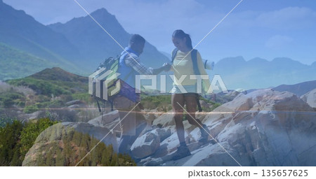 Hiking couple helping each other stepping down in rugged mountains, with yellow and camo backpacks Hiking couple helping each other stepping down in rugged mountains, with yellow and camo backpacks 135657625