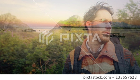 Standing traveler wearing padded jacket and backpack at lakeside sunset, with boats, copy space 135657628