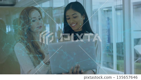 Collaborating two tech professionals wearing blazer examining laptop in office with network overlay Collaborating two tech professionals wearing blazer examining laptop in office with network overlay 135657646