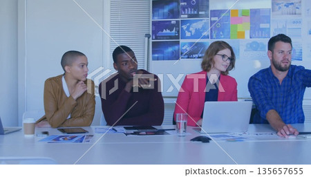 Collaborating business team analyzing charts at conference room table, with laptop tablet screens 135657655