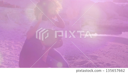 Balancing couple on sandy beach, woman wearing striped top and denim shorts, holding smartphone Balancing couple on sandy beach, woman wearing striped top and denim shorts, holding smartphone 135657662