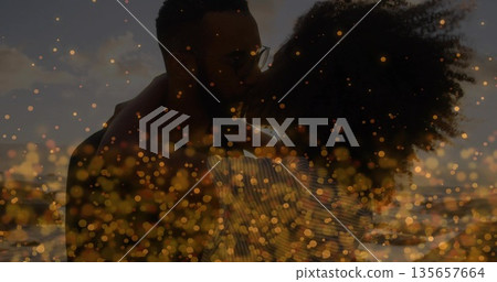 Embracing couple wearing striped top, dark shirt with eyeglasses on beach at sunset, bokeh effect 135657664