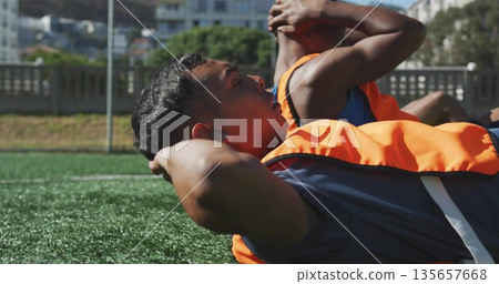 Performing sit-up exercises soccer players lying on turf field, with training bibs, athletic shorts Performing sit-up exercises soccer players lying on turf field, with training bibs, athletic shorts 135657668